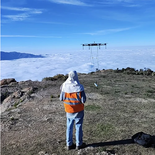 Image of geophysicist flying a drone at high altitude, from a mountaintop with the cloud layer below.